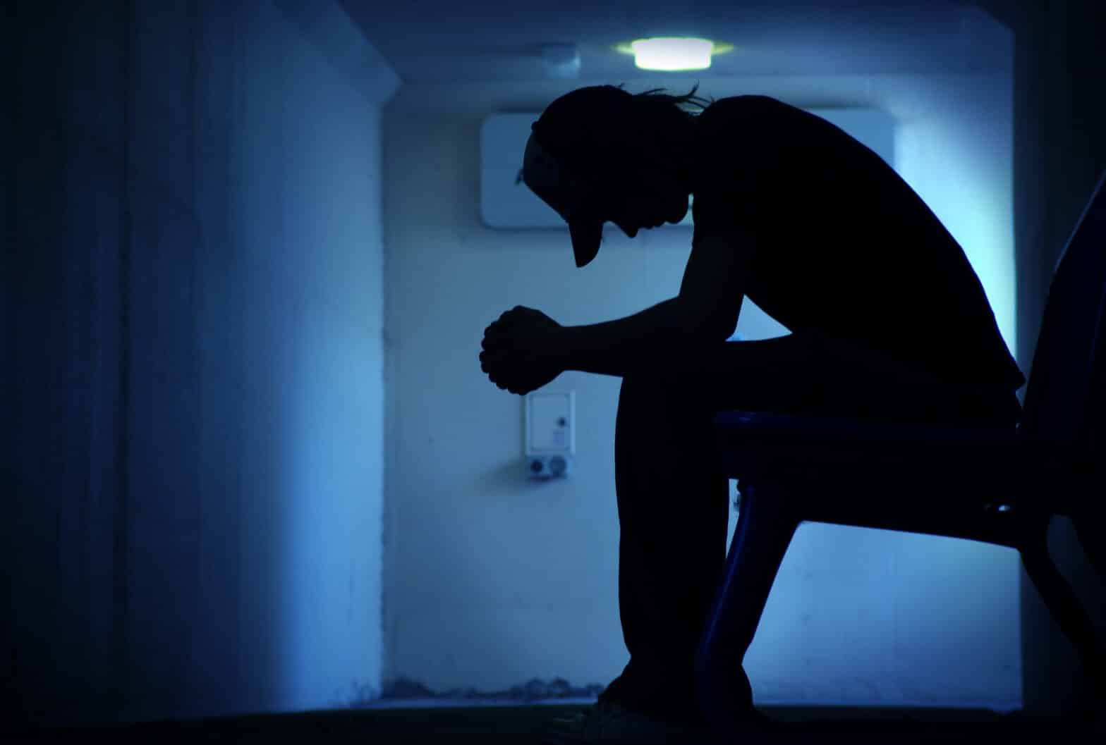 A silhouette of a young man sitting in a dark hallway - Hitting Rock Bottom And Getting Addiction Treatment
