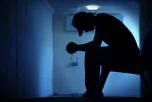 A silhouette of a young man sitting in a dark hallway - Hitting Rock Bottom And Getting Addiction Treatment