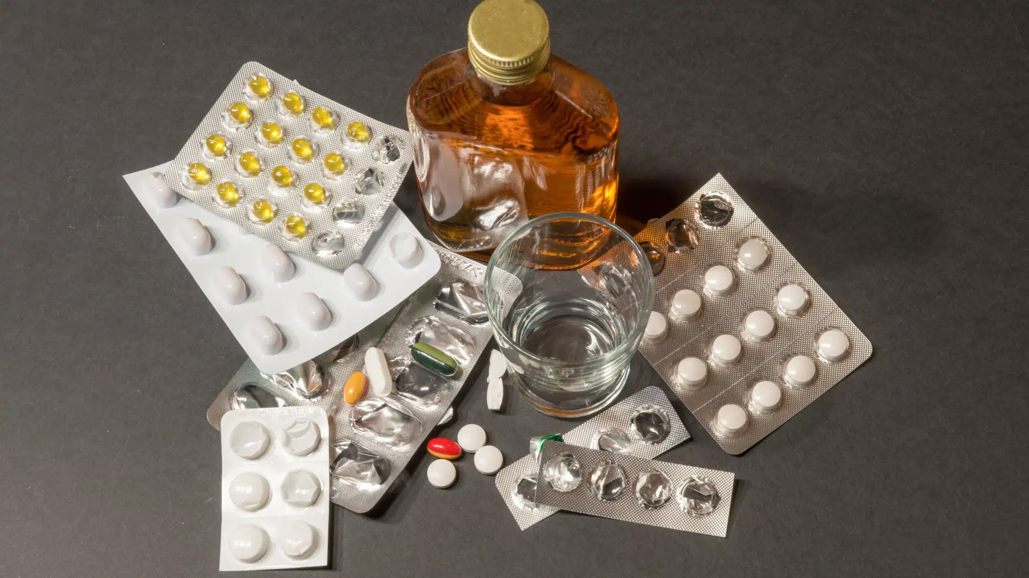 Pills surround a bottle of alcohol - 5 Signs You May Be Self-Medicating