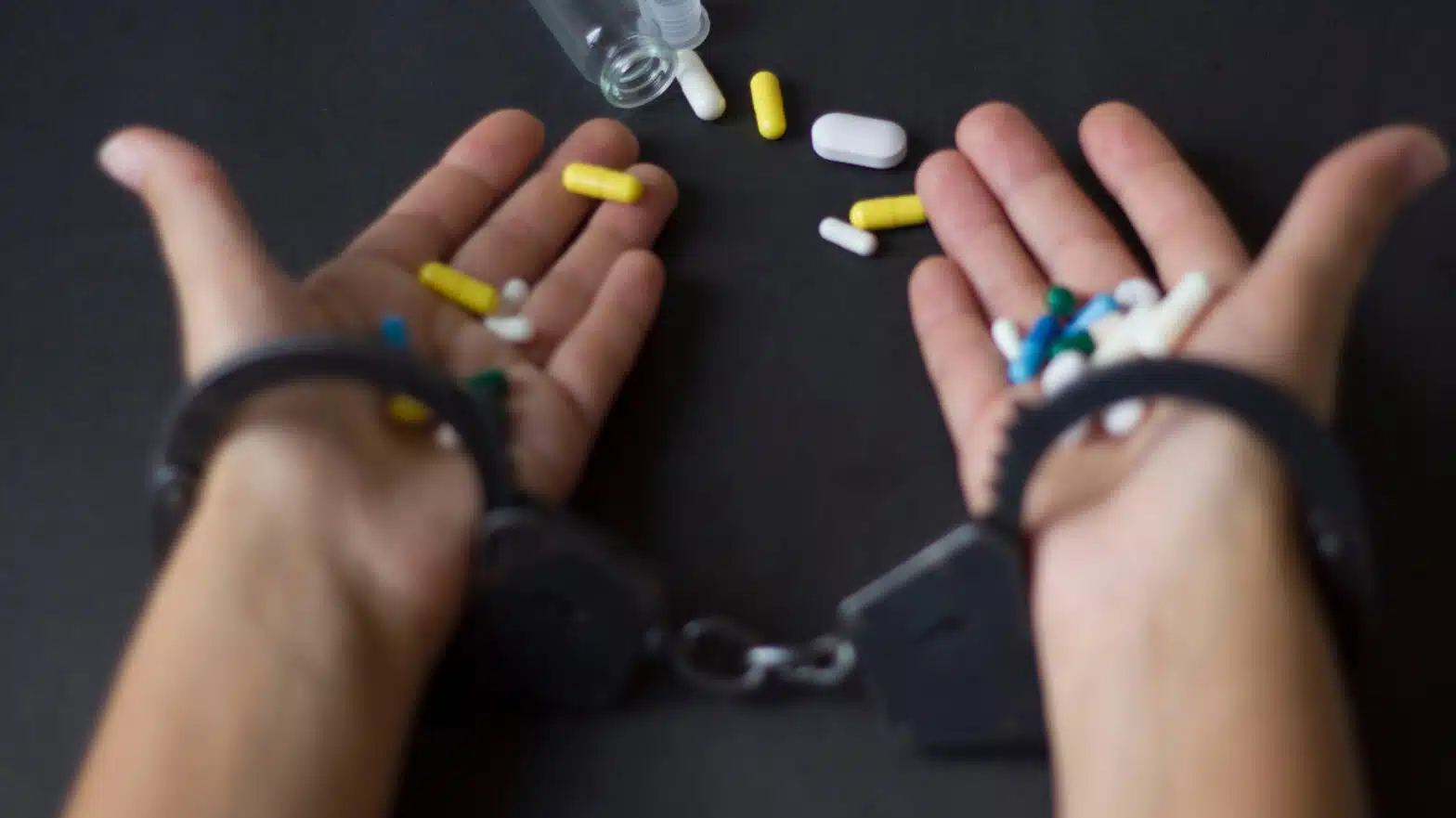 A person in handcuffs holds pills in both hands - Can I Get Into Legal Trouble For Admitting Drug Use In Rehab