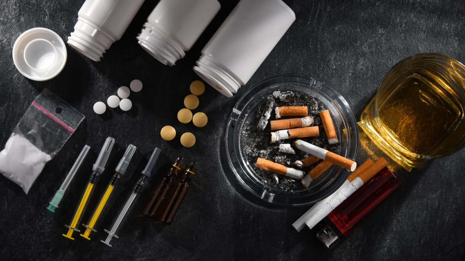 A collection of pills, cigarettes, syringes, and a glass of whiskey - Why Do People Get Addicted To Drugs