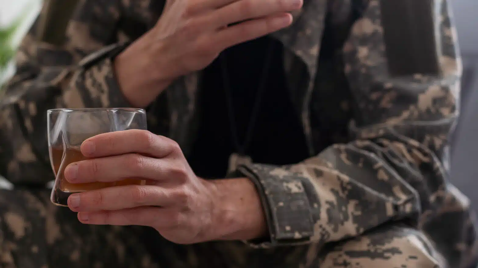 a man in military fatigues holds a glass of liquor - Quality Of Addiction Treatment In The Military