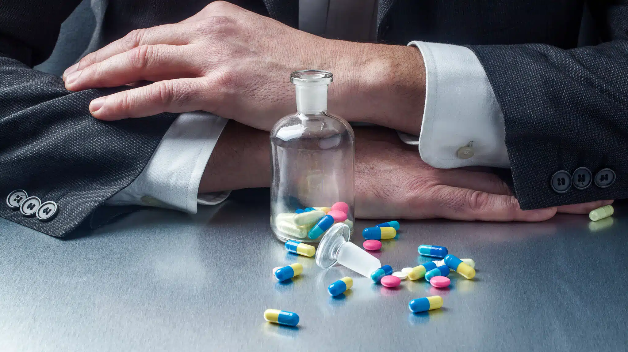 A pill bottle is on a table in front of a man in a suit - Professions With High Addiction Rates