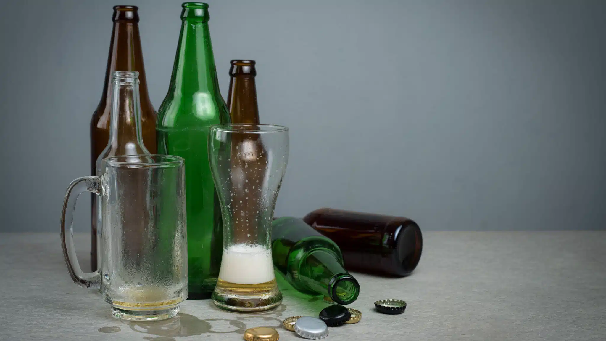 A collection of empty beer bottles, a glass, and a mug - 10 Signs Of Drinking Too Much
