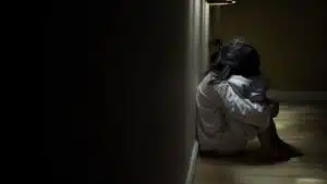 A young girl sits alone on the floor of a dark hallway - Substance Abuse In The Foster Care System