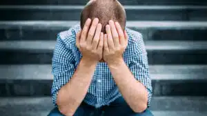 A man sitting on stairs rests his head in his hands - What Is The Abstinence Violation Effect (AVE)