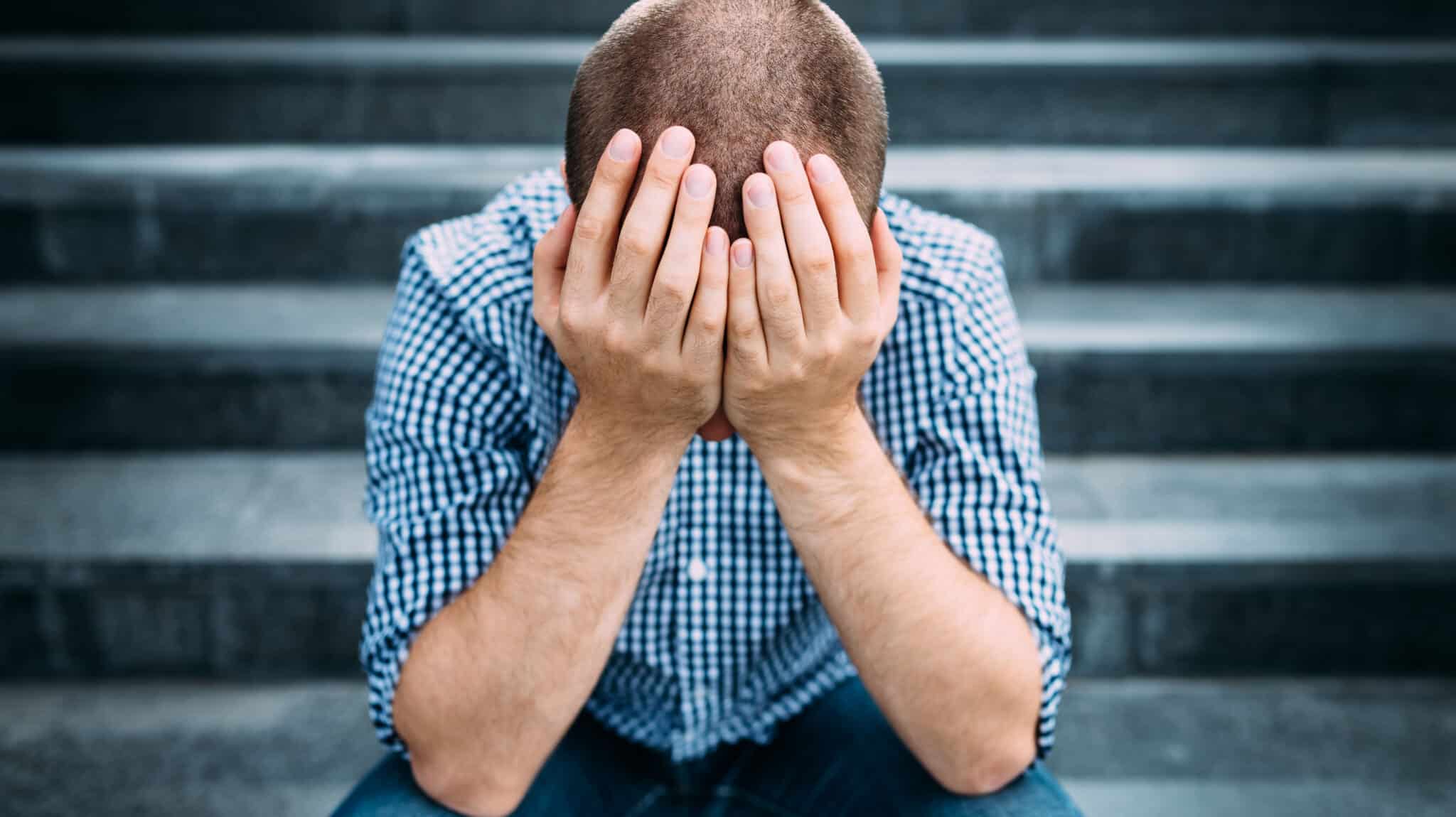 A man sitting on stairs rests his head in his hands - What Is The Abstinence Violation Effect (AVE)